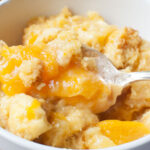 An upclose view of crockpot peach cobbler with a spoon in it.