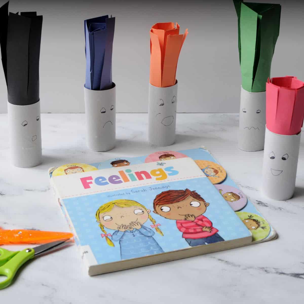 book about feelings and then toilet paper rolls made to look like people with faces. They have construction paper hair and there are safety scissors near them. 