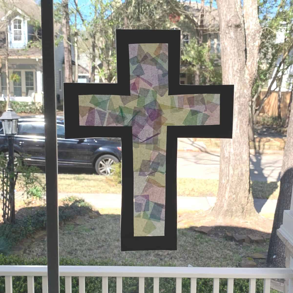 Tissue paper cross craft hanging in a window.
