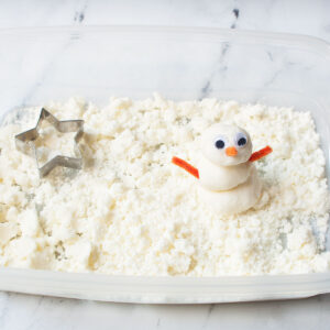 snow dough in a sensory bin there's a snowman and a cookie cutter