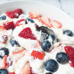 A spoon scooping triple berry cheesecake fruit salad.