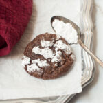 A chocolate Christmas crinkle cookie with a spoon of powdered sugar next to it.