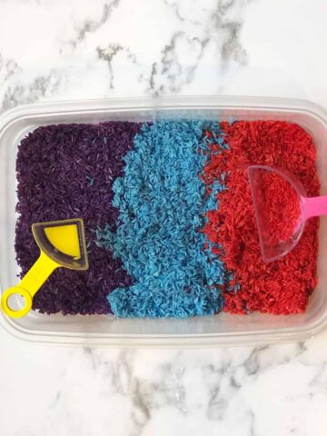 sensory bin with dyed rice with measuring cups in it