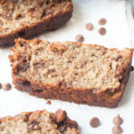 A slice of Chocolate Chip Oatmeal Banana Bread surrounded by chocolate chips.