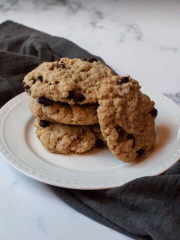 Copycat Otis Spunkmeyer Oatmeal Raisin Cookies stacked on a white plate with a gray linen