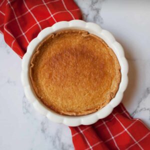 copycat cracker barrel buttermilk pie in a white pie pan with a red linen