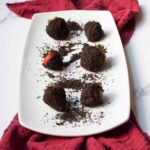 Chocolate Oreo Covered Strawberries on a rectangle plate with a red linen and Oreo crumbles
