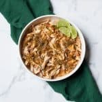 Crockpot Shredded Salsa Chicken with limes in a white bowl with a green linen