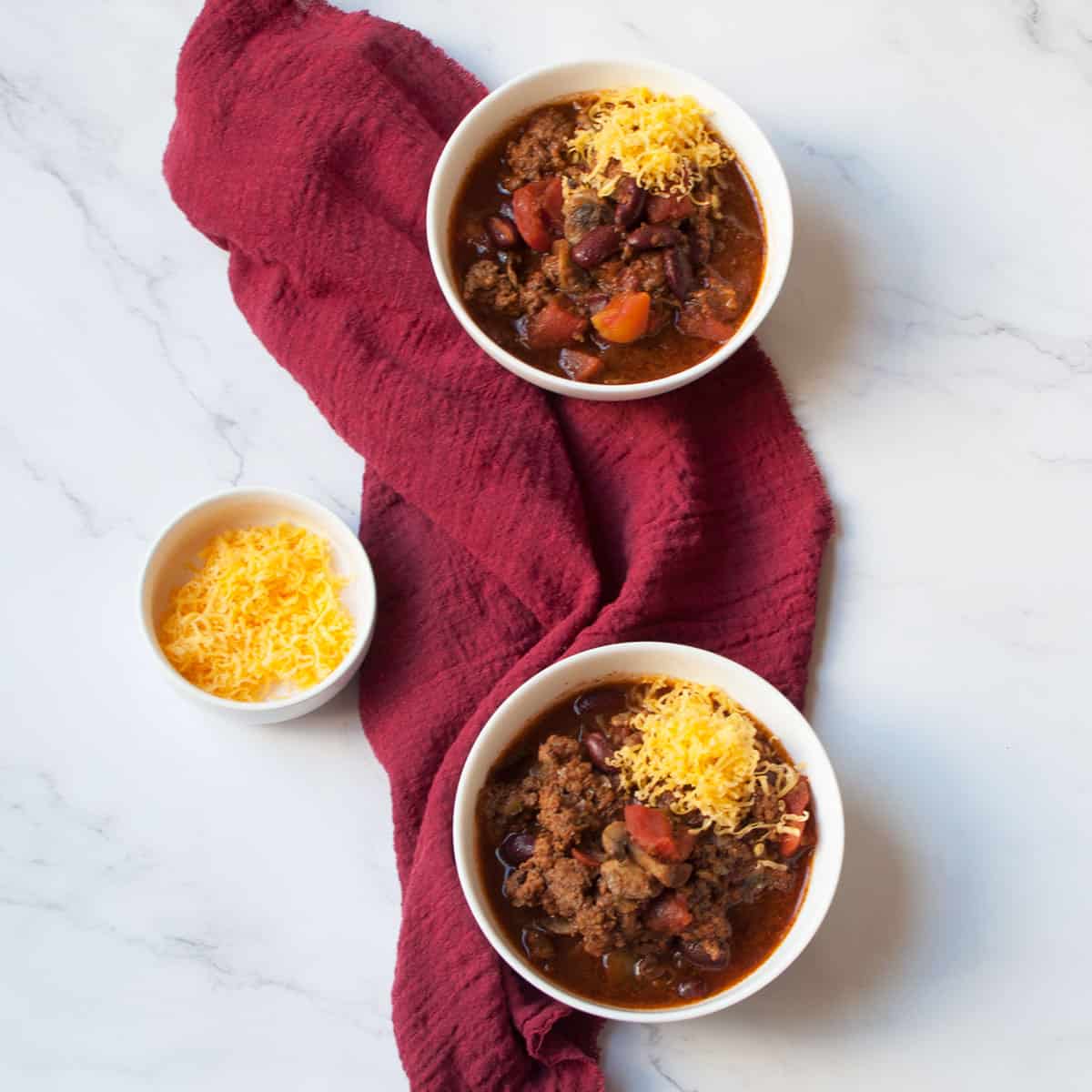 Copycat Tim Horton's Chili in two bowls with a red linen and a bowl of cheese