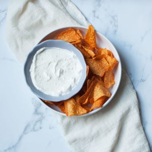 Dip for doritos in a gray bowl surrounded by doritos in a white bowl