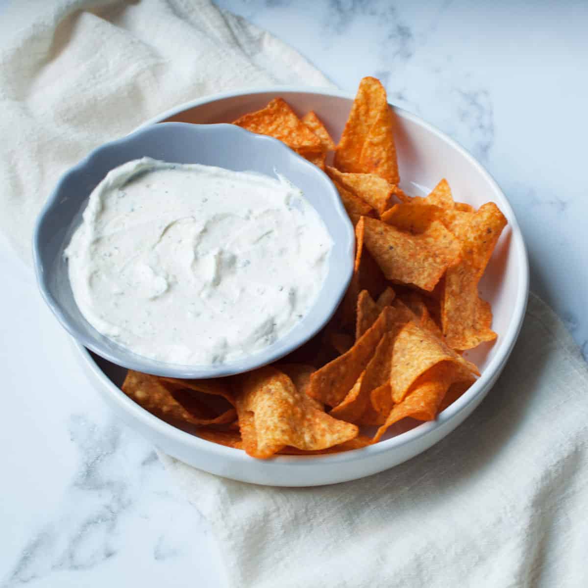 Dip for doritos in a gray bowl surrounded by doritos in a white bowl