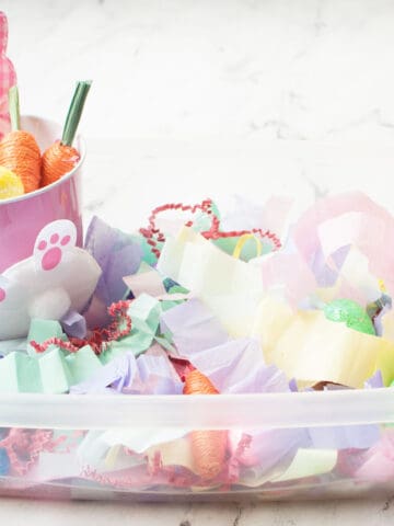 An Easter themed sensory bin made from shredded tissue paper and small egg and carrot toys.