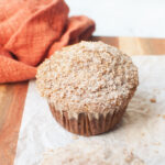 A sourdough discard pumpkin muffin on a wooden board with an orange linen.