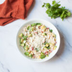 mexican street corn salad in a white bowl with an orange linen and cilantro beside it