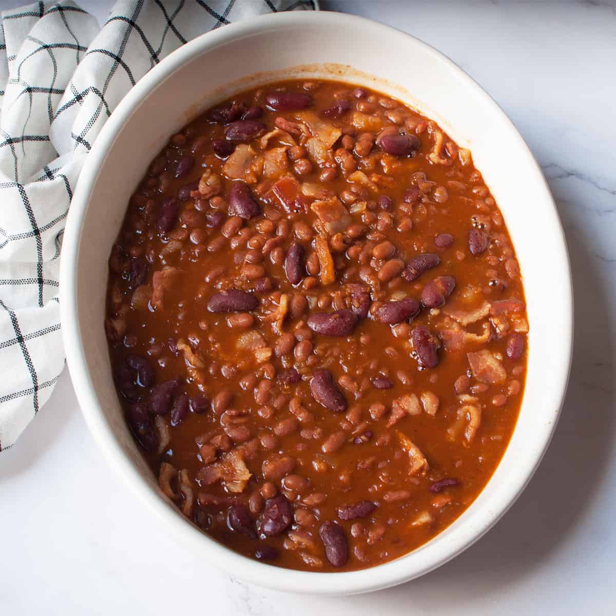 Dr Pepper Baked Beans in a white oval dish with a white and black linen near it. 