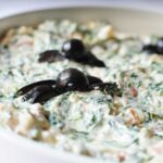 close up shot of halloween spinach dip with olive spiders