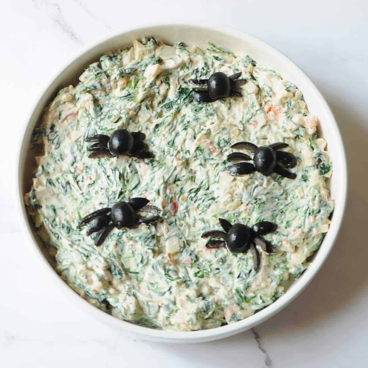 spinach dip with olives that were cut out to look like spiders in it 