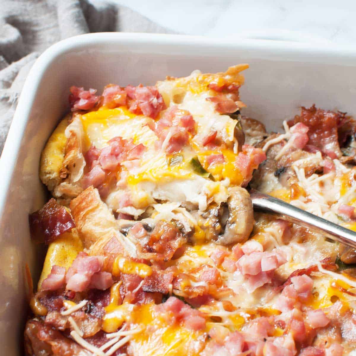 an image of a breakfast casserole (croissants, cheese, ham, bacon, mushrooms, and egg) in a casserole dish. 