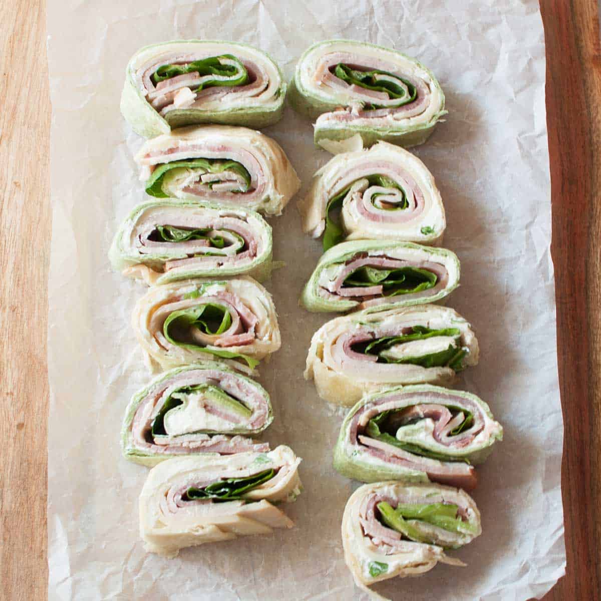 pin wheel sandwiches (sandwiches made from tortillas, lunch meat, cream cheese mixture, and lettuce) on a wooden tray