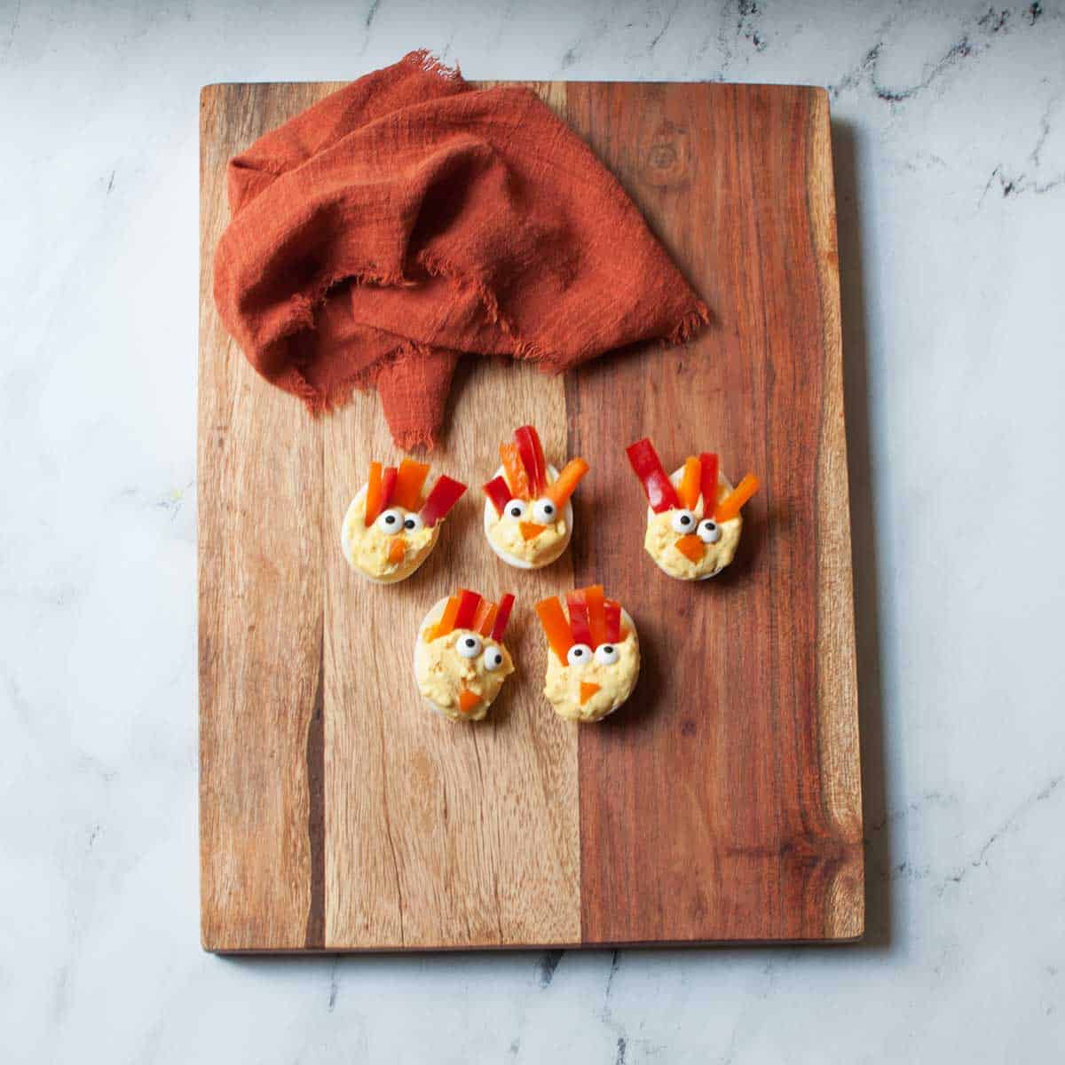 deviled eggs that have candy eyes and bell pepper strips arranged to make them look like turkeys on a wooden tray