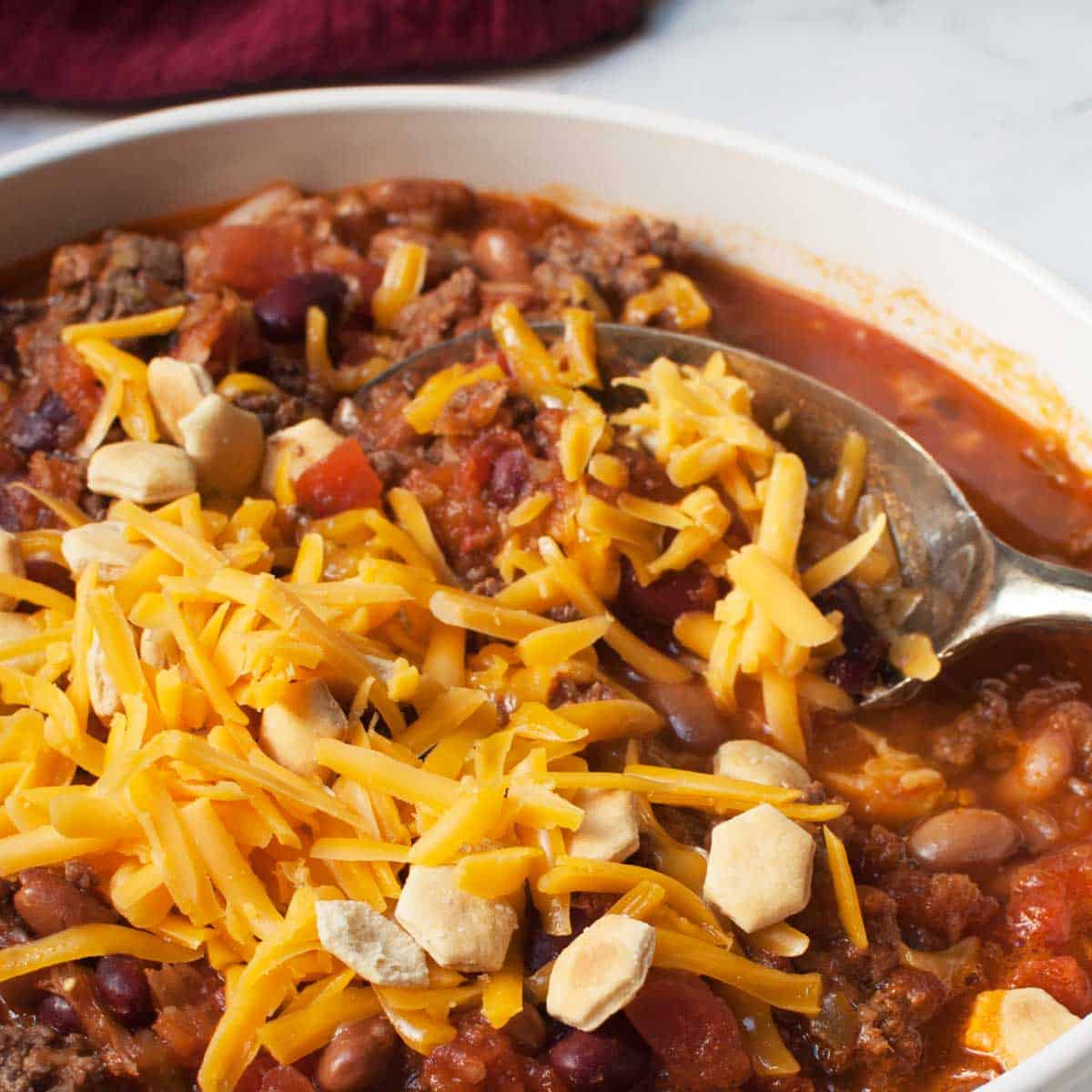 A spoon scooping Copycat Wendy's Chili  that has cheese and crackers on it. 