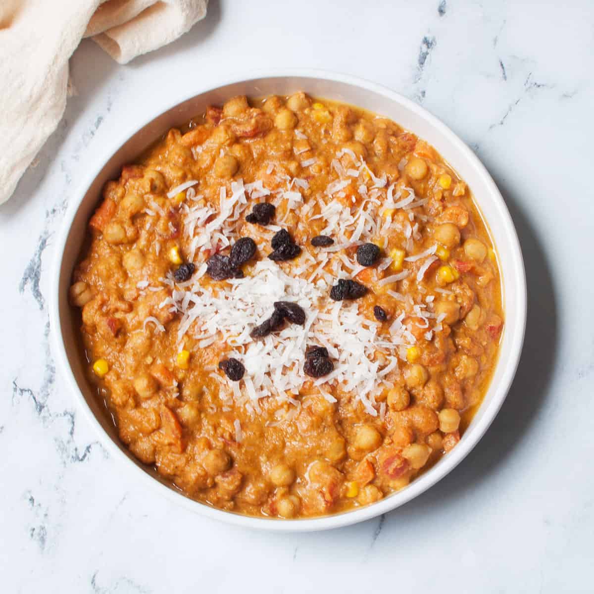 Pumpkin Chickpea Curry in a white dish with coconut flakes and raisins on it