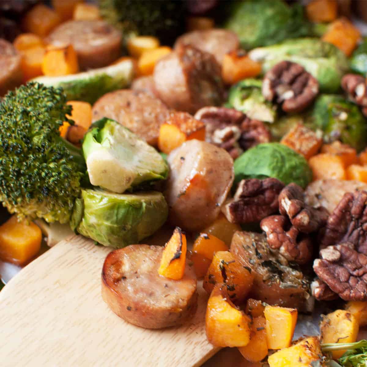 Harvest Sheet Pan Dinner (apple sausage, butternut squash, pecans, broccoli, and brussels sprouts) on a sheet pan. There is a spoon scooping it.