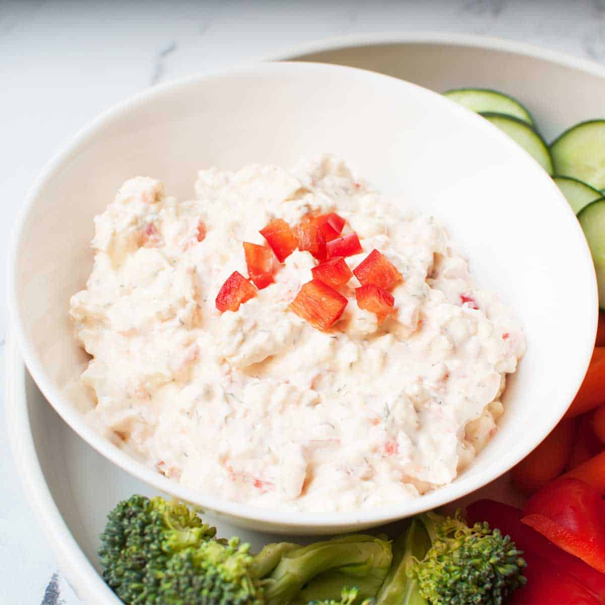 cream cheese dip in a bowl with red bell peppers that have been diced on top of it