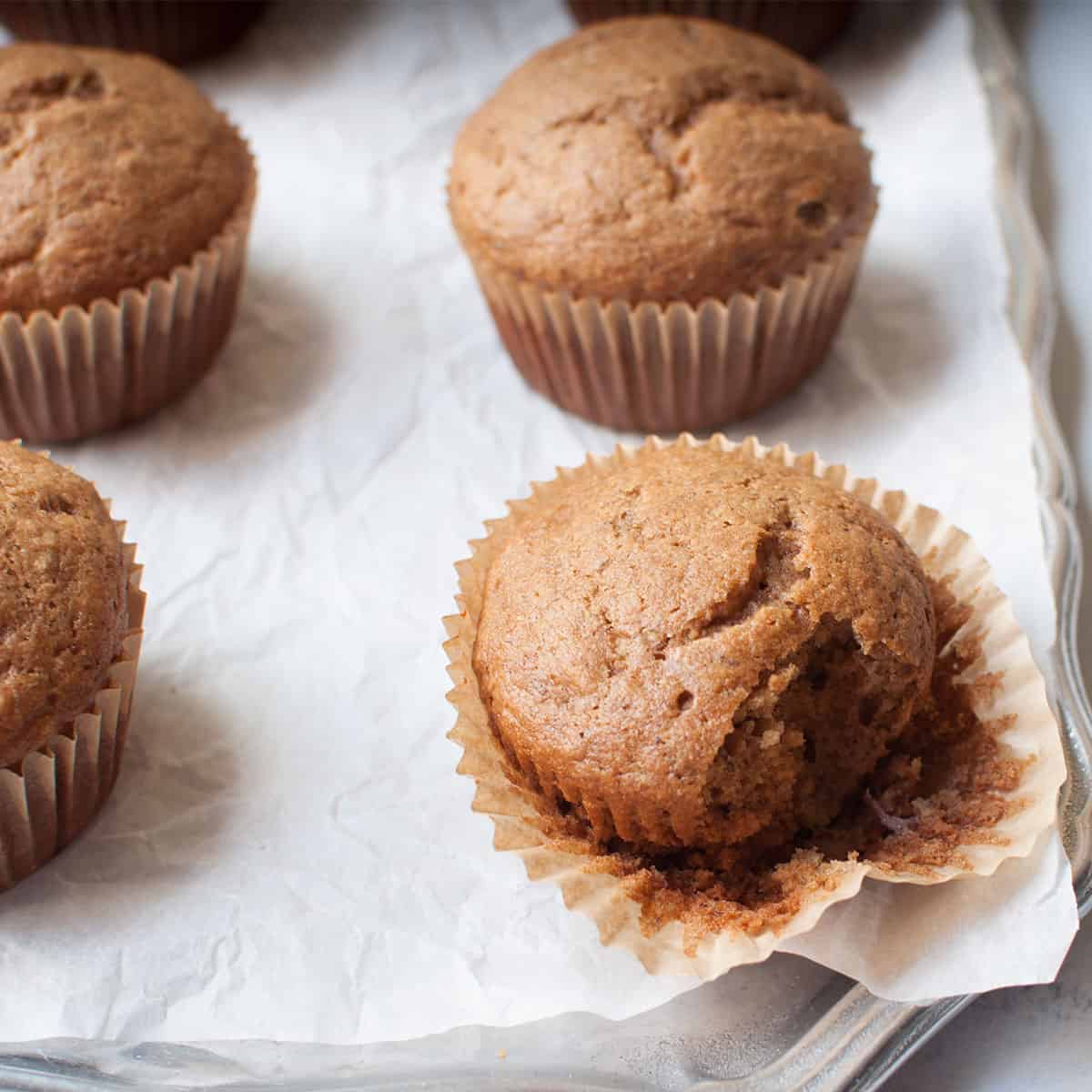 banana muffins on parchment paper, one has a bite taken out of it. 