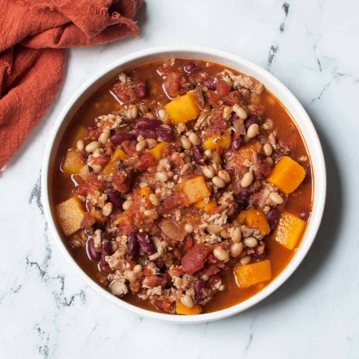 a bowl of Crockpot Turkey Chili with Butternut Squash with an orange linen near it