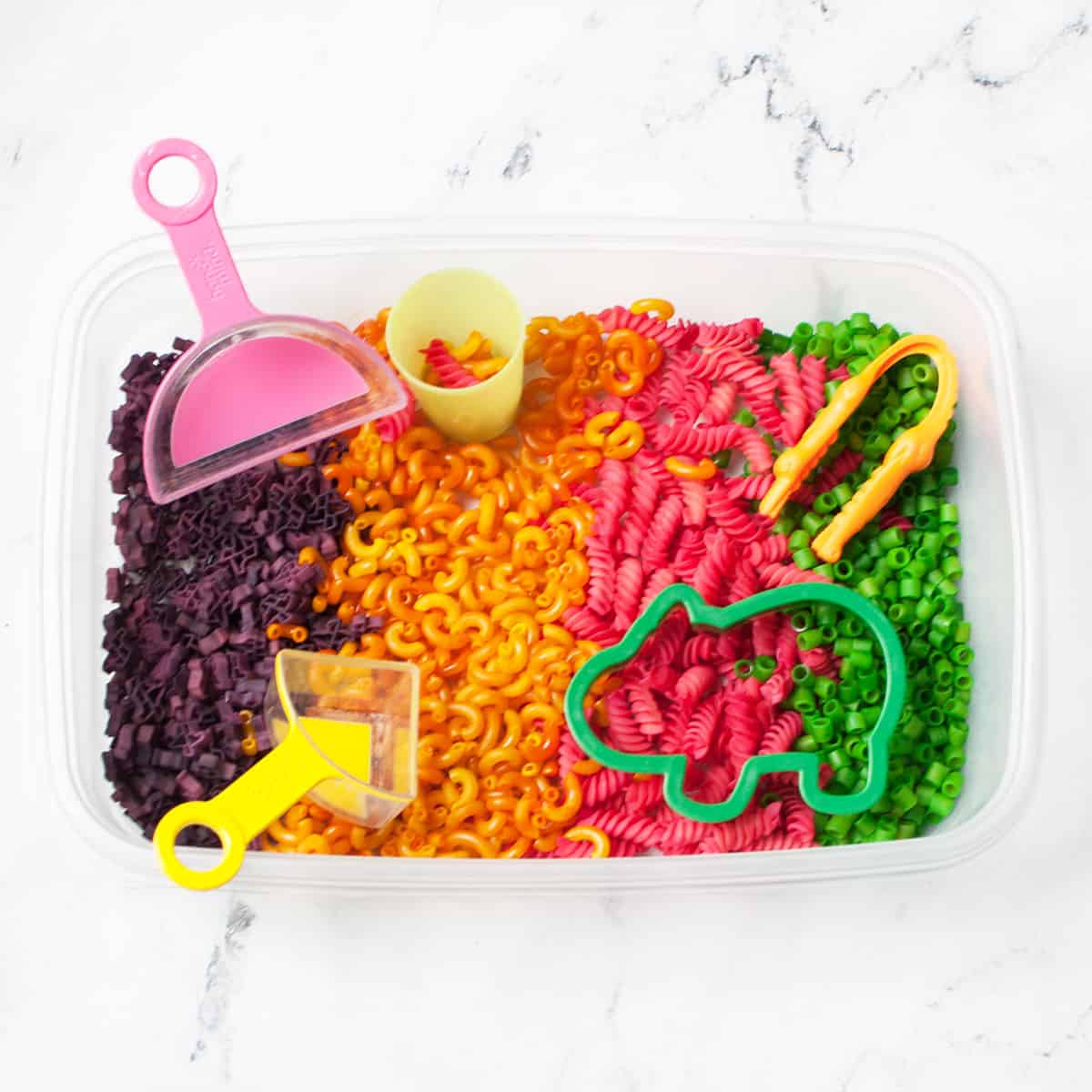 a sensory bin filled with dyed pasta, scoops, and toys