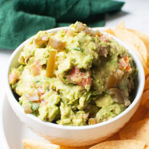 guacamole with pickled jalepenos in a bowl surrounded by tortilla chips