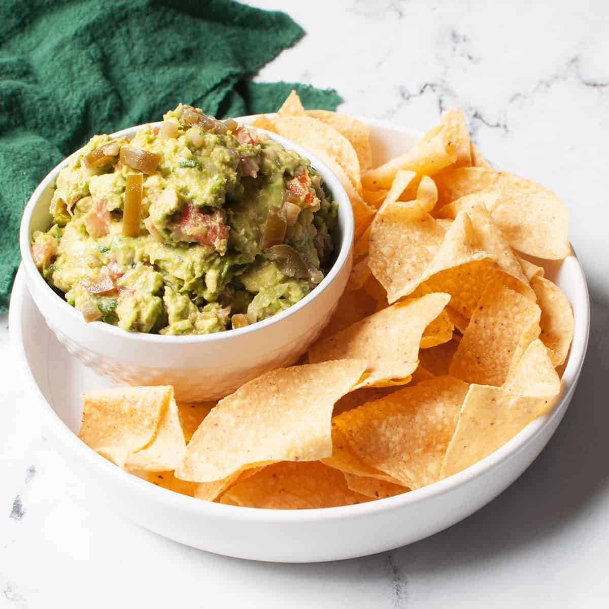 guacamole with pickled jalepenos in a bowl surrounded by tortilla chips
