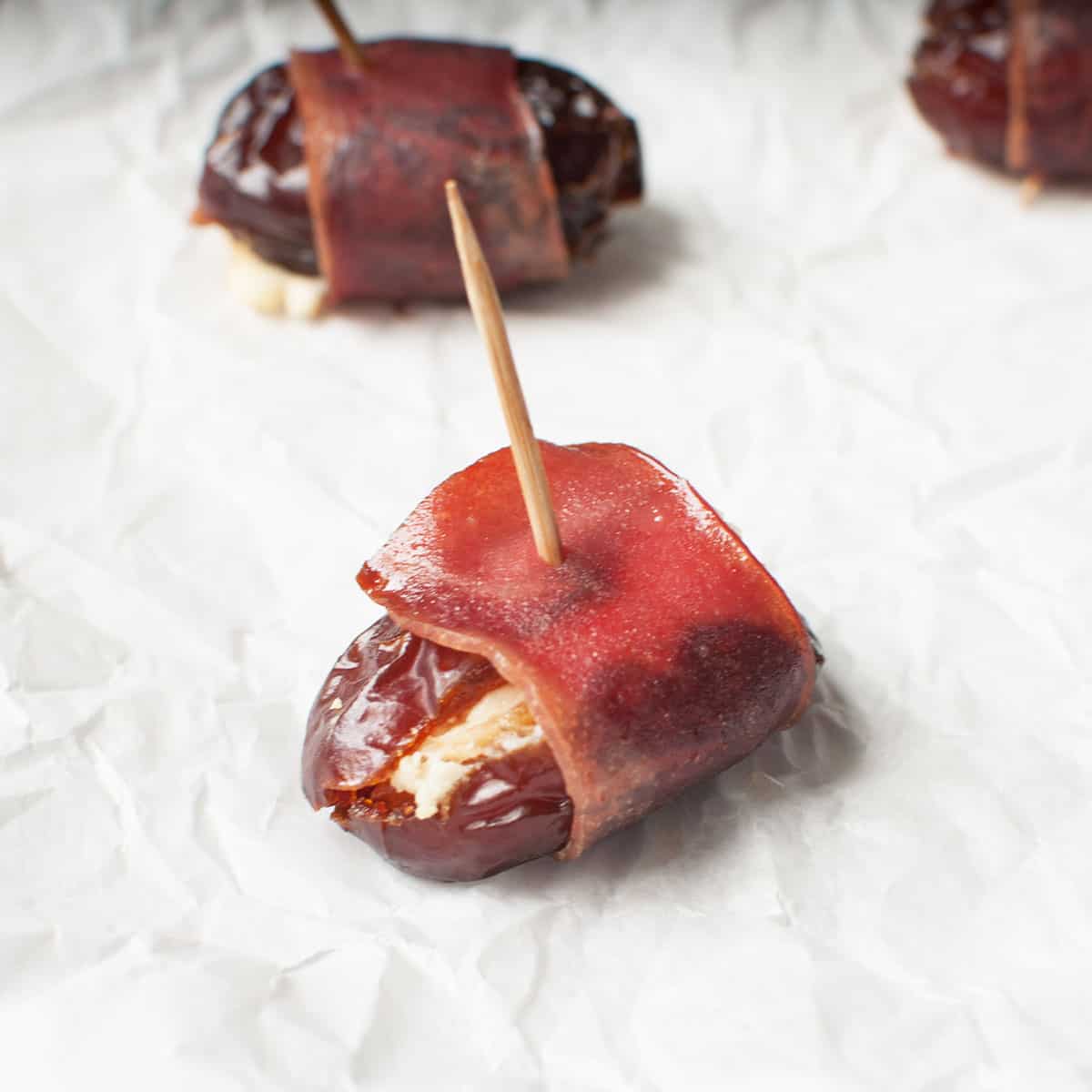 A close up view of a turkey bacon wrapped date with a toothpick in it.