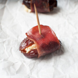A close up view of a date wrapped in turkey, stuffed with goat cheese, with a toothpick in it.