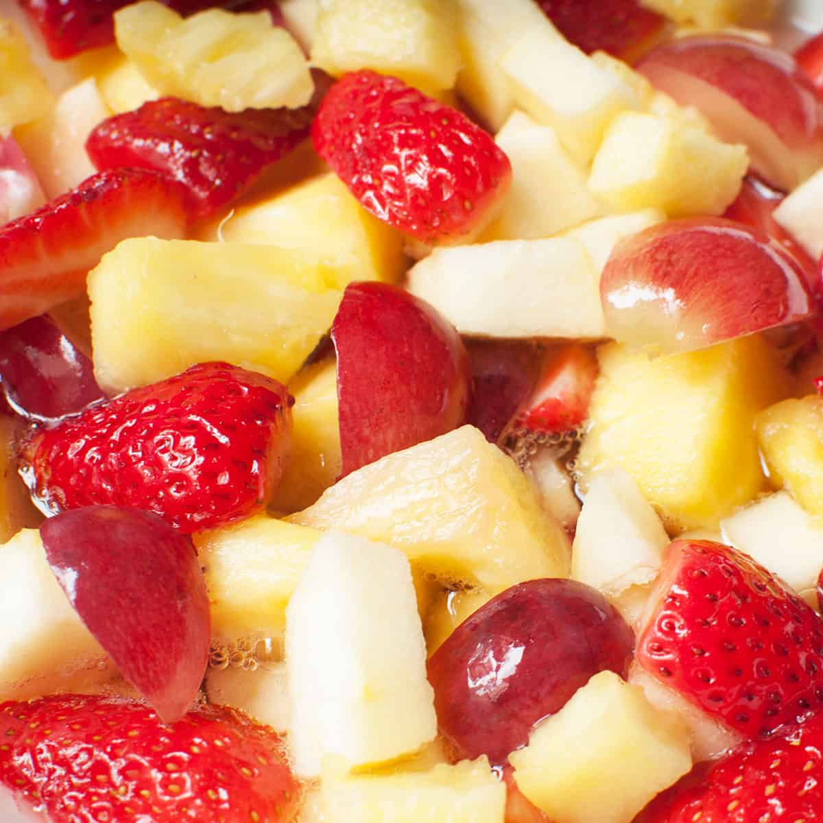 A close up view of fruit salad with Sprite. There are grapes, apple slices, pineapple chunks, and strawberries. 