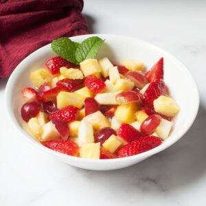 Fruit salad with Sprite in a white bowl with mint leaves on top of it.