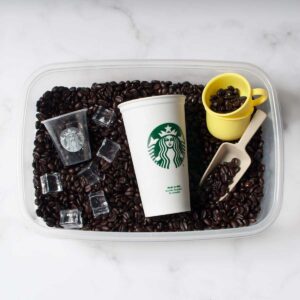 A coffee bean sensory bin with cups, scoops, and toy ice cubes in it.