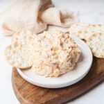 A scoop of Copycat Chicken Salad Chick Buffalo Barclay chicken salad on a white plate on a wooden board with crackers.