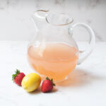 Copycat Wendy's Strawberry Lemonade in a pitcher with a lemon and two strawberries by it.