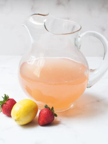 Copycat Wendy's Strawberry Lemonade in a pitcher with a lemon and two strawberries by it.