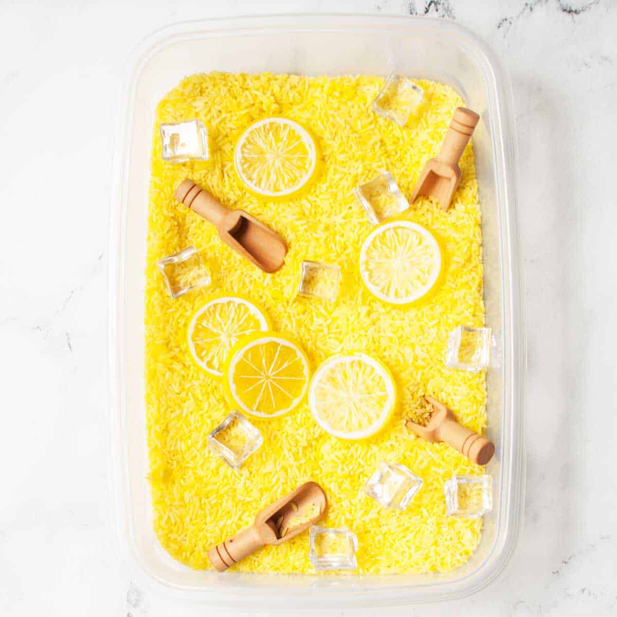 A lemonade sensory bin (rice dyed yellow with toy lemon slices, ice cubes and wooden scoops).