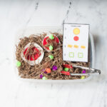 A pizza sensory bin made from crinkled paper, pizza, and pompoms. There is a pizza order card and tongs in the bin too.