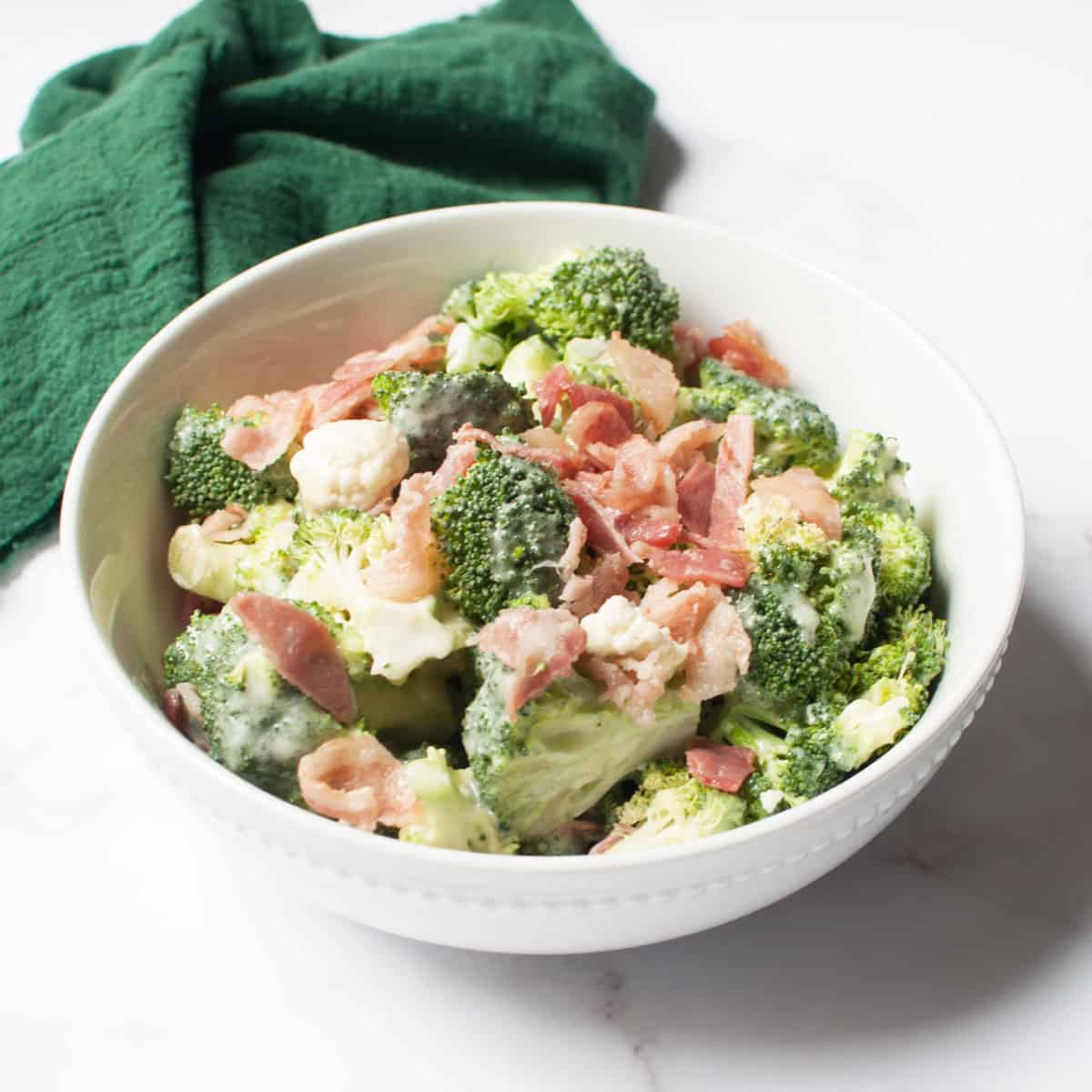 Amish Broccoli and Cauliflower Salad in a white bowl with a green linen.