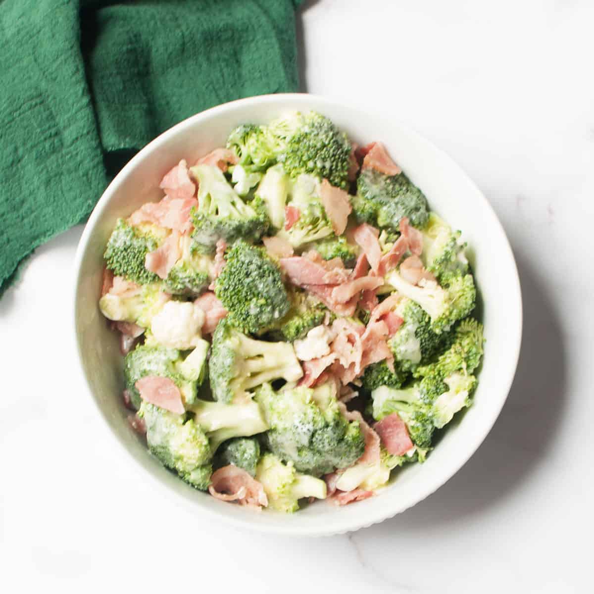 Amish Broccoli and Cauliflower Salad in a white bowl with a green linen.