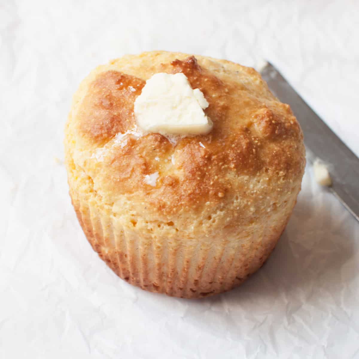 Jumbo corn muffin with butter on it. There is a butterknife in the background.