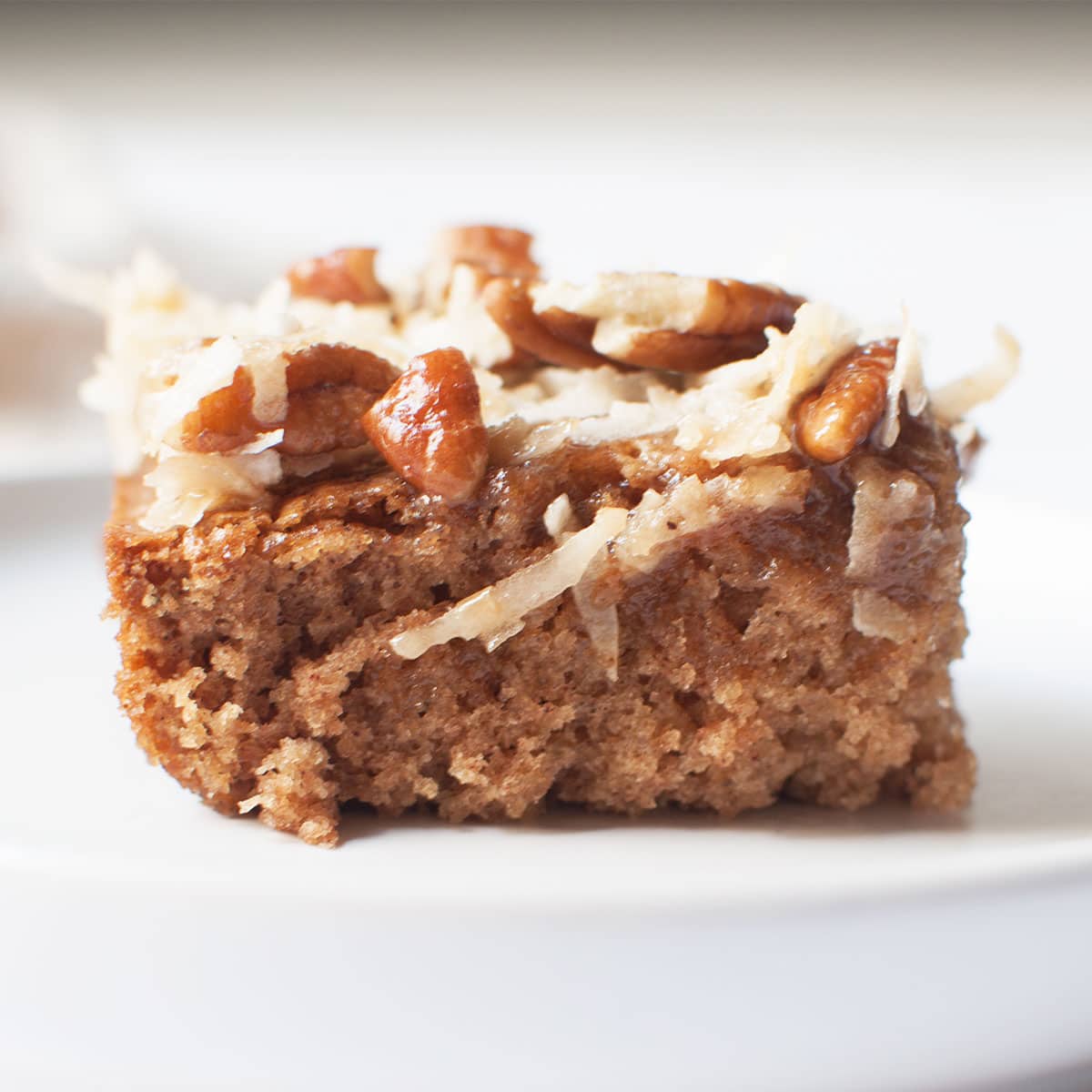 A slice of Amish cake on a white plate (oatmeal cake with a coconut pecan topping).