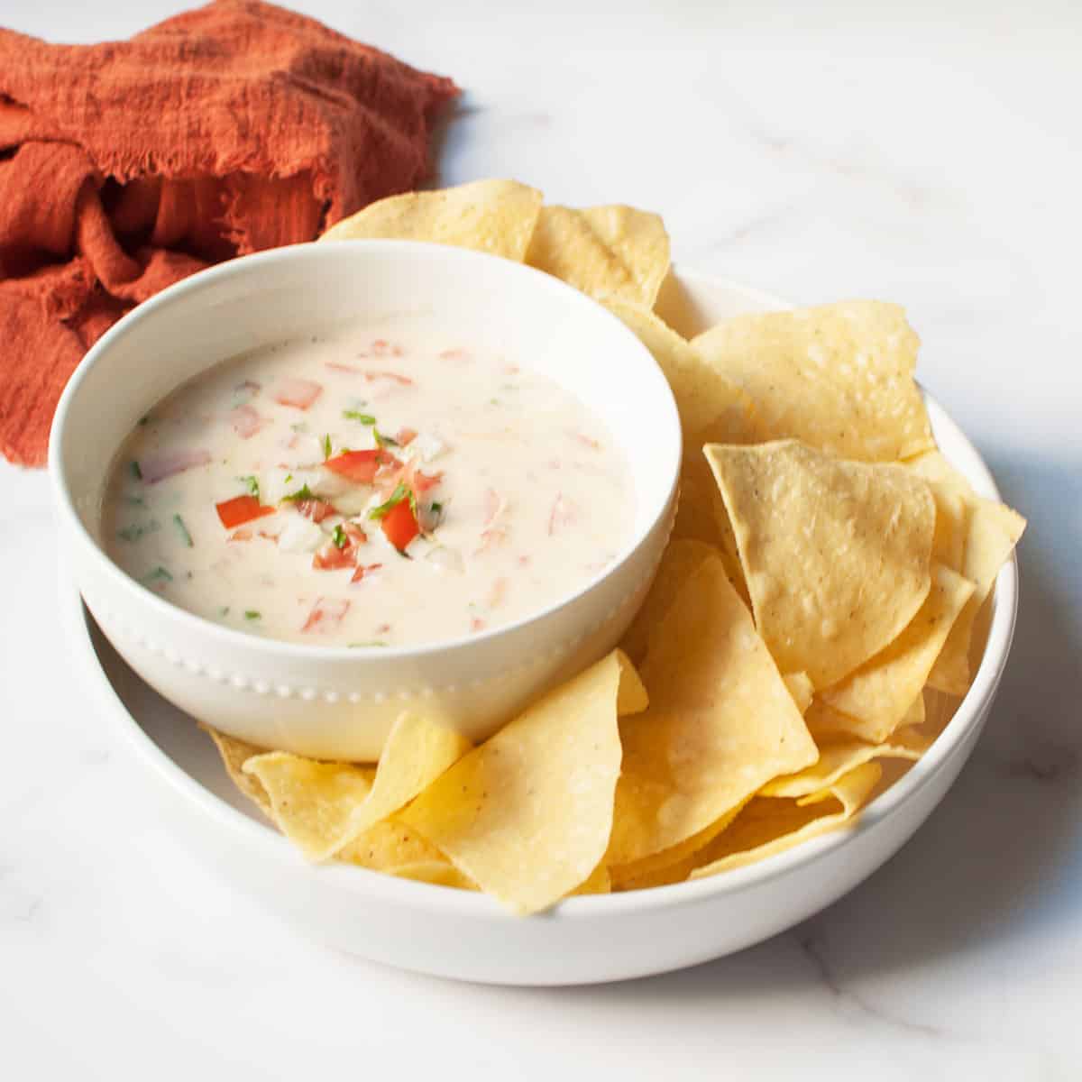 Copycat Freebirds Queso in a white bowl surrounded by tortilla chips.
