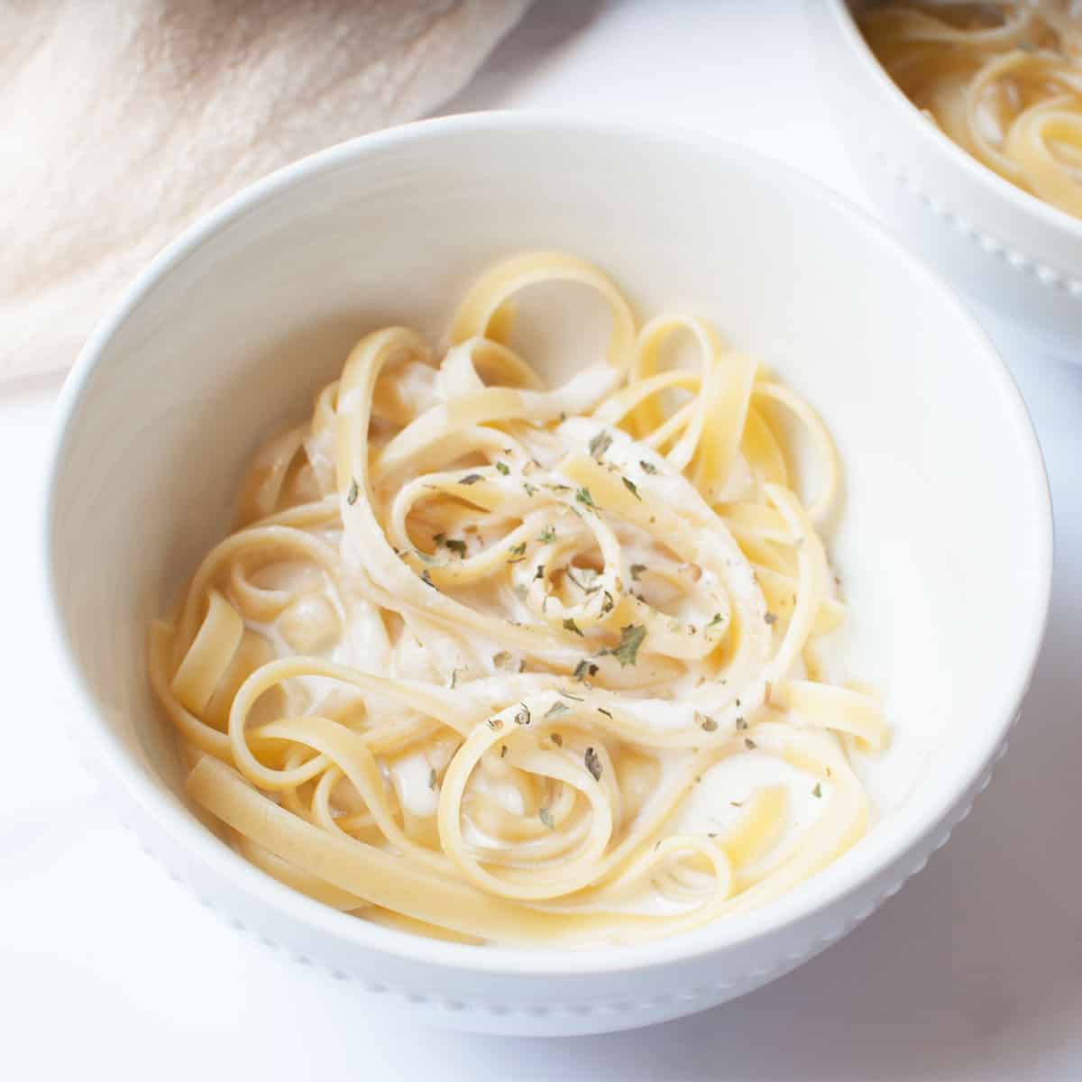 A white bowl with alfredo and fettucini pasta in it. 