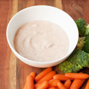 Mexican ranch in a white bowl with carrots and broccoli by it.